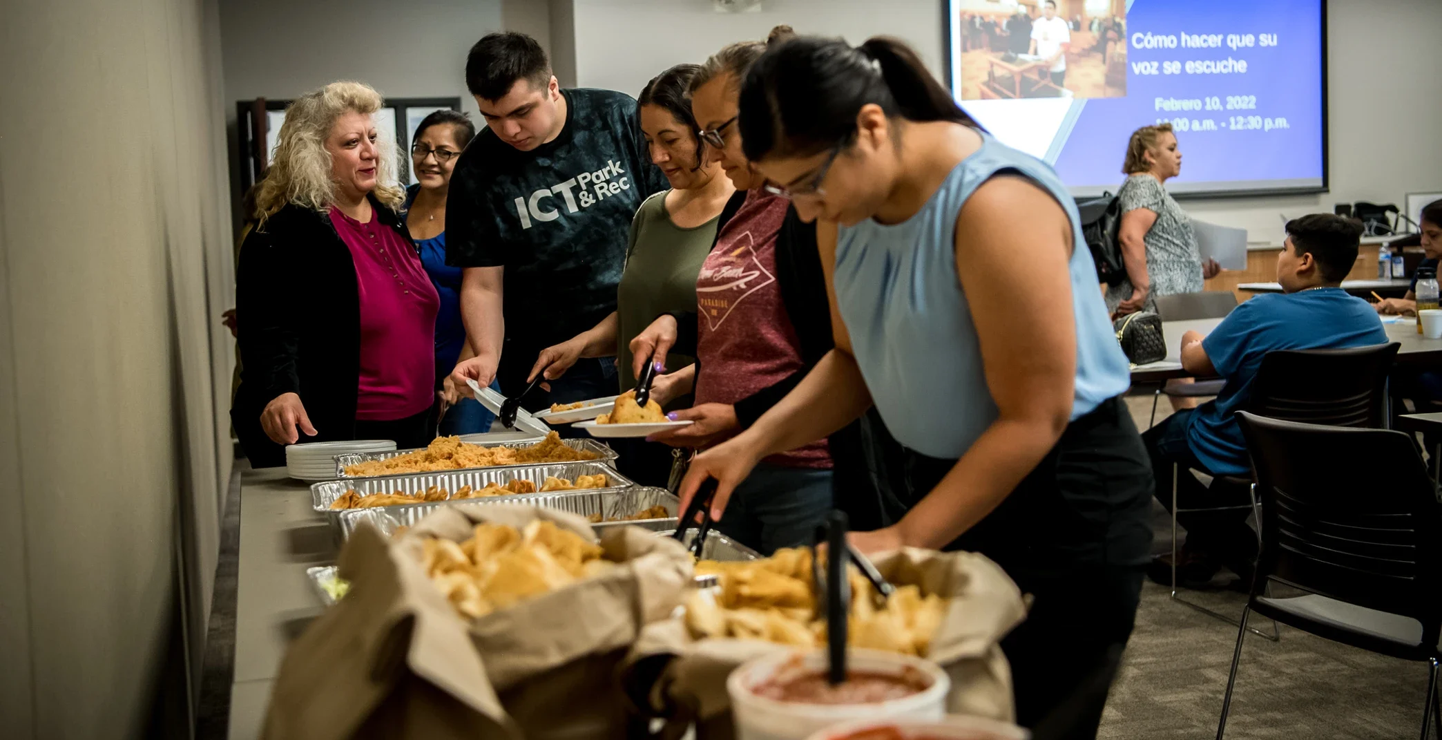 People get food from a buffet line at an Alce su Voz event